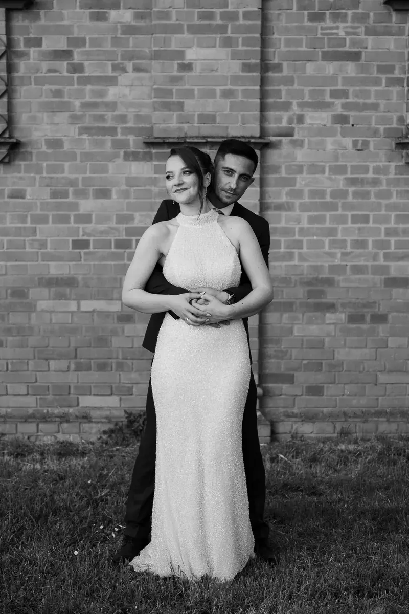 Mladenci u nježnom zagrljaju ispred opečnog zida, crno-bijela umjetnička fotografija vjenčanja u Vinkovcima.