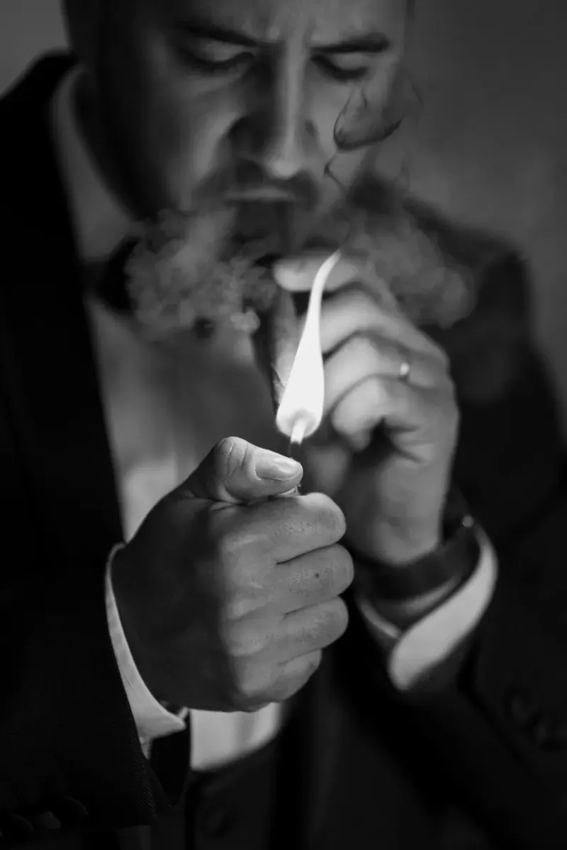 Mladoženja pripaljuje cigaru u intimnom crno-bijelom kadru prije svadbene proslave.