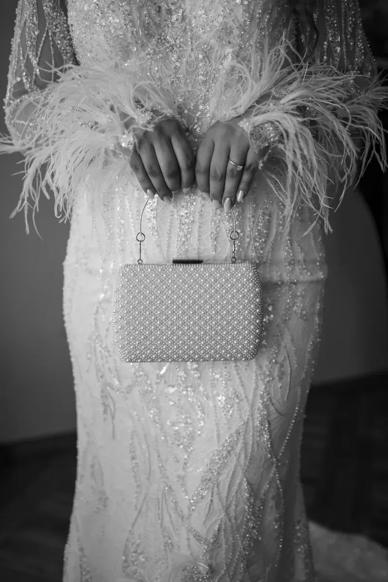 Elegantna torbica ukrašena biserima u rukama mladenke, detalj uz vjenčanicu s perlicama.