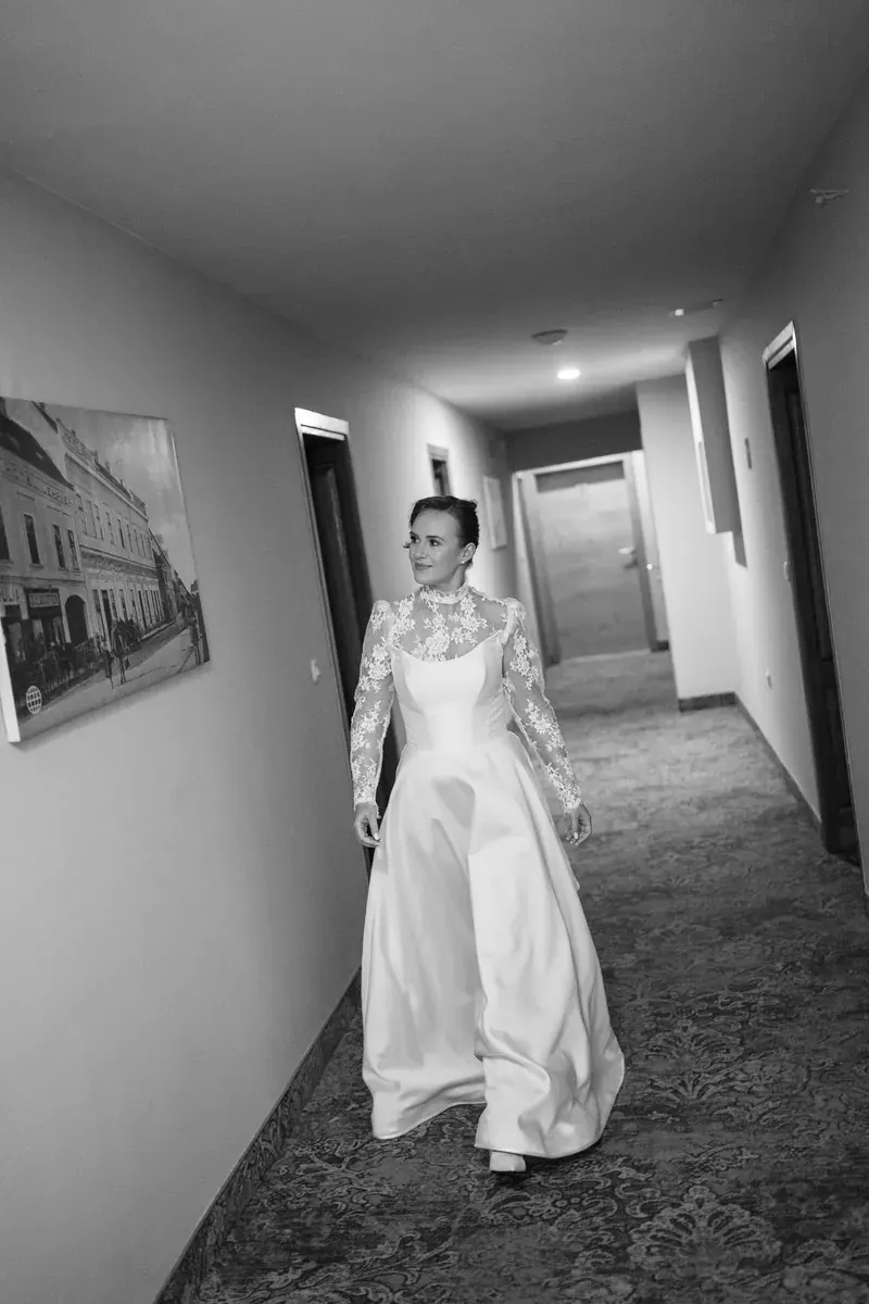 Mladenka hoda hotelskim hodnikom u vjenčanici, osvrćući se s osmijehom preko ramena.